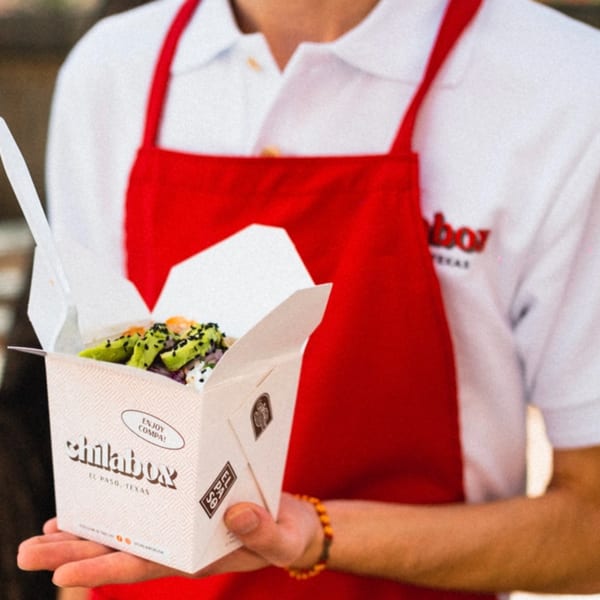 A person in a red apron holds an open Chilabox takeout container filled with food.