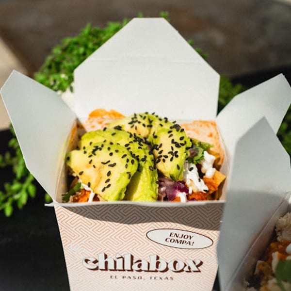 Chilabox takeout container filled with Mexican food, topped with avocado slices and black sesame seeds.