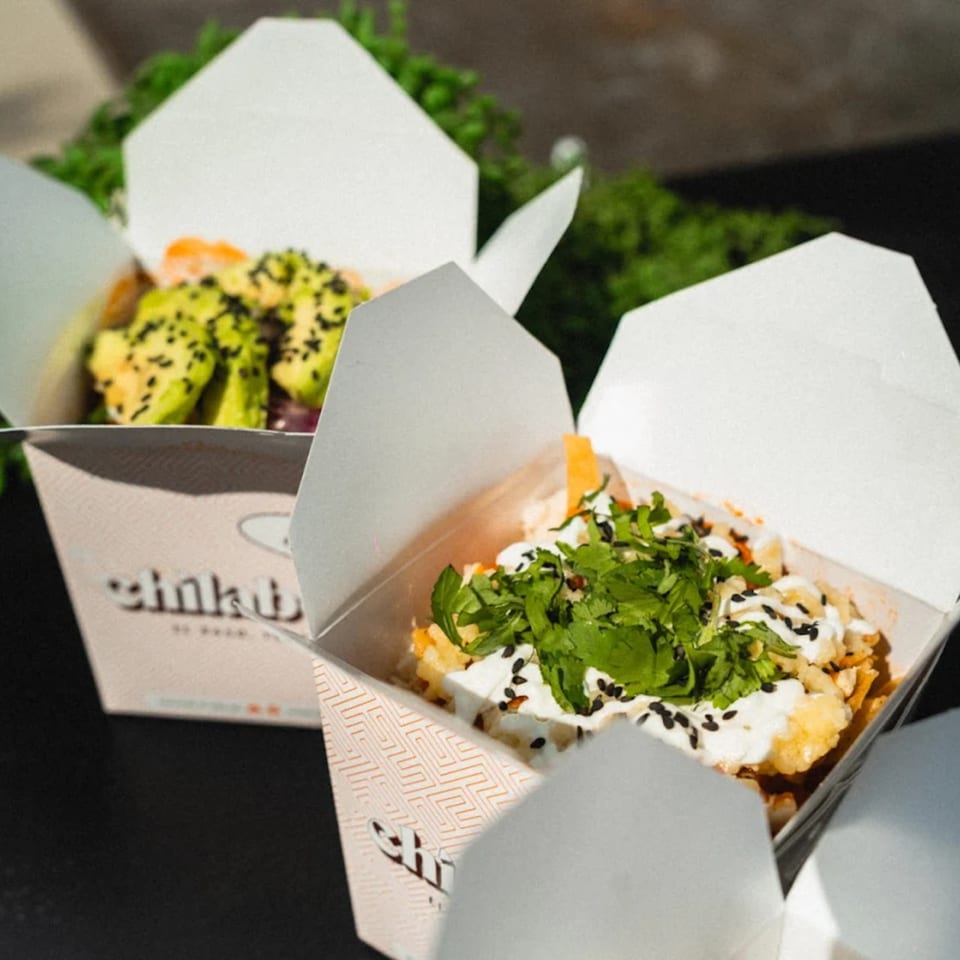 Two Chilabox takeout containers filled with Mexican food, one with avocado and the other with cilantro.