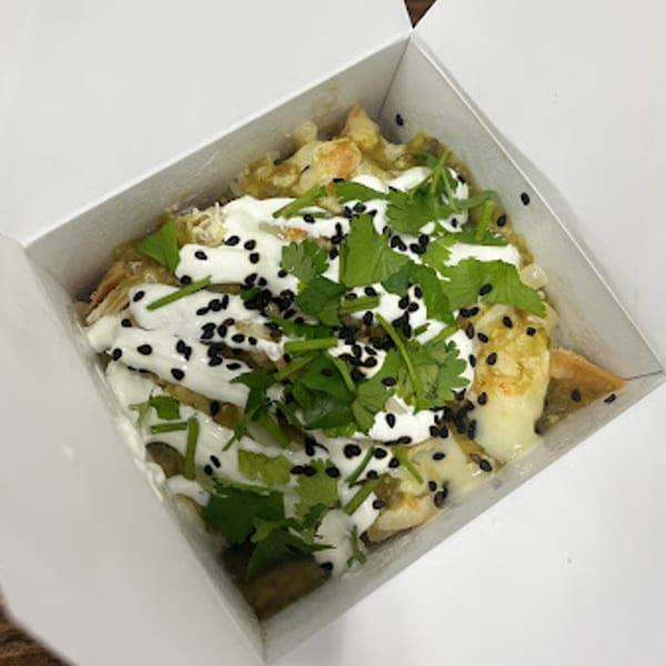 Chilabox chilaquiles with green sauce, sour cream, cilantro, and black sesame seeds in a white box.