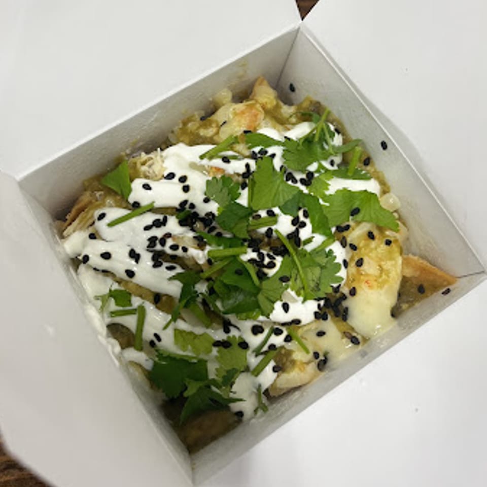Chilabox chilaquiles with green sauce, sour cream, cilantro, and black sesame seeds in a white box.