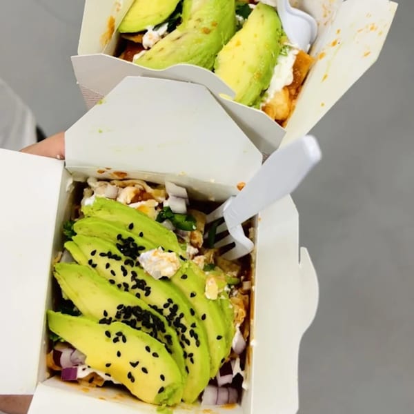 Two Chilabox chilaquiles with avocado slices, black sesame seeds, and a plastic fork.
